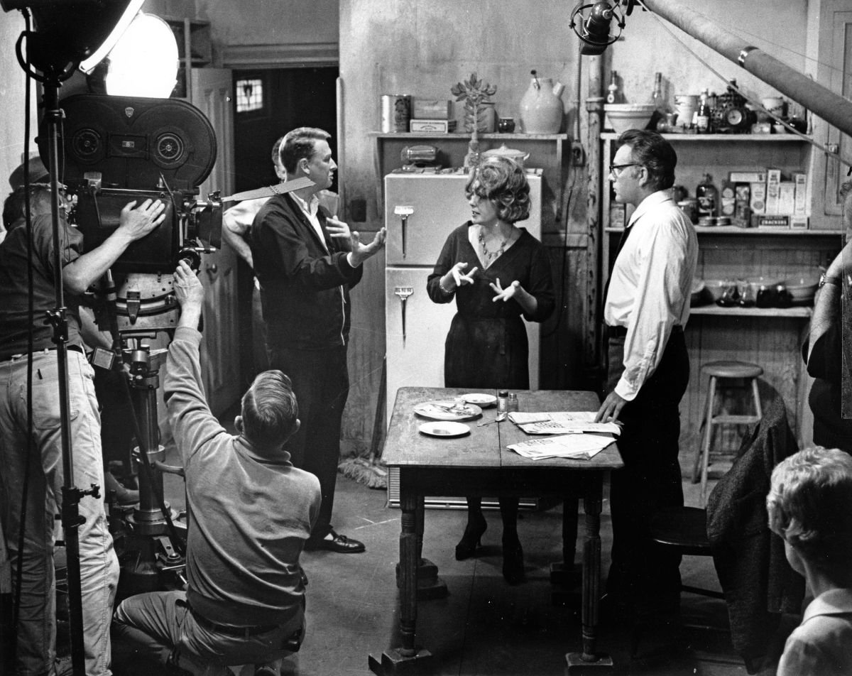 Director Mike Nichols confers with his stars. The kitchen was lit realistically to look flat and drab. Single cone light mounted overhead was used as key with very little fill from the floor and no attempt to gobo light with flags and cutters. Flat lighting in this sequence also provided visual variety, because the bulk of film is photographed with light of harsh contrast.