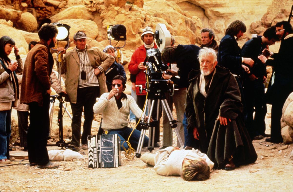 Cinematographer Gilbert Taylor, BSC (grasping a light stand at left) observes as the Star Wars crew, and actors Alec Guinness and Mark Hamill, prepare for a take on location in Tunisia. “The trouble with the future in most futurist movies is that it always looks new and clean and shiny,” director George Lucas (second from left) told AC in July 1977. “What is required for true credibility is a used future. The Apollo space capsules were instructive in that regard. By the time the astronauts returned from the moon, the capsules were littered with… candy wrappers and old Tang jars, no more exotic than the family station wagon.”